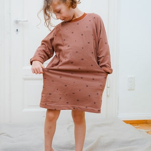 May include: A brown dress with a black geometric pattern. The dress has long sleeves and a round neckline. The dress is made of a soft, comfortable fabric.