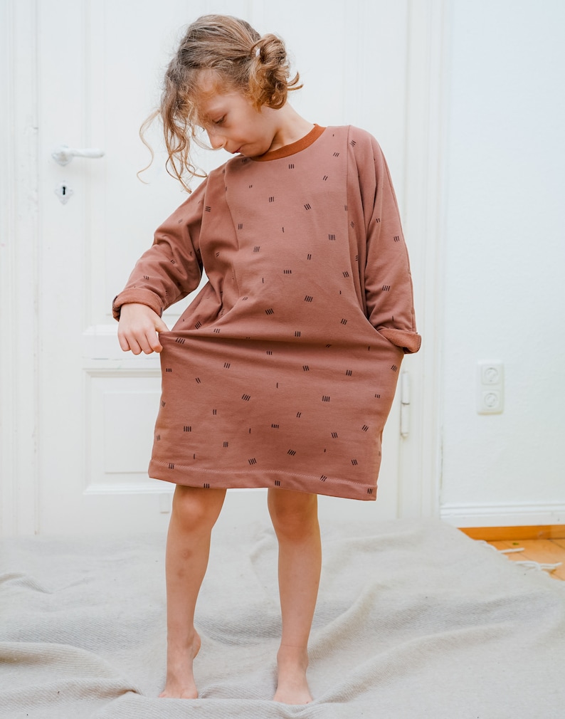 May include: A brown dress with a black geometric pattern. The dress has long sleeves and a round neckline. The dress is made of a soft, comfortable fabric.