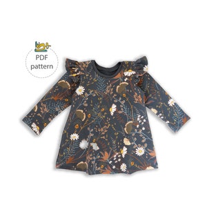 May include: A dark grey long-sleeved dress with a floral print featuring white daisies, brown leaves, and yellow accents. The dress has a ruffled neckline and sleeves.