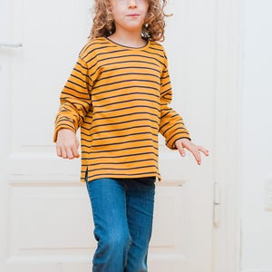 Puede incluir: Un ni&ntilde;o con una camisa de manga larga a rayas amarillas y negras y pantalones vaqueros azules.