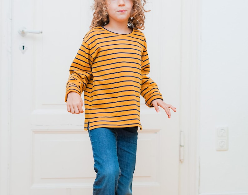 Puede incluir: Un ni&ntilde;o con una camisa de manga larga a rayas amarillas y negras y pantalones vaqueros azules.