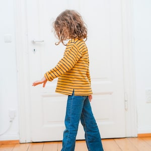 Puede incluir: Un ni&ntilde;o con una camisa de manga larga a rayas amarillas y azules y pantalones vaqueros azules.
