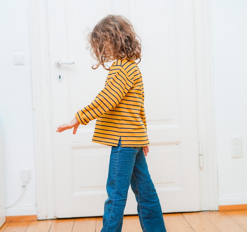 Puede incluir: Un ni&ntilde;o con una camisa de manga larga a rayas amarillas y azules y pantalones vaqueros azules.