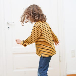 Puede incluir: Un ni&ntilde;o con una camisa de manga larga a rayas amarillas y azul marino y pantalones vaqueros azules.