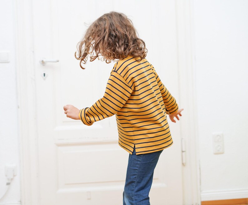Puede incluir: Un ni&ntilde;o con una camisa de manga larga a rayas amarillas y azul marino y pantalones vaqueros azules.