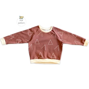 May include: A brown long-sleeved sweatshirt with a white triangle pattern and a cream-colored ribbed neckline and cuffs.
