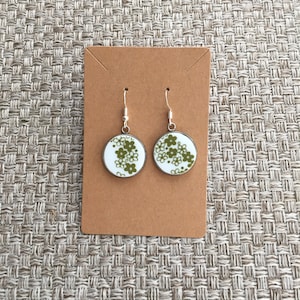 Puede incluir: Un par de pendientes de plata con dijes redondos de cerámica blanca con un patrón floral verde.