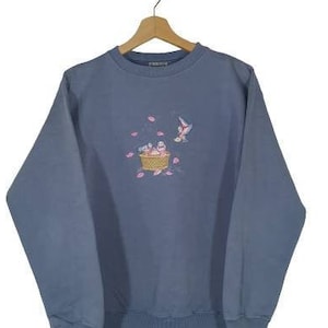 May include: A light blue long-sleeved sweatshirt with an embroidered design of birds in a basket with pink flowers.