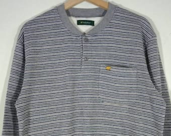 May include: Gray striped long-sleeve shirt with a single button placket and a small yellow logo on the pocket. The shirt has a ribbed crew neck.