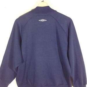 Pu&ograve; includere: Una felpa blu navy con un logo a forma di diamante bianco sul retro.