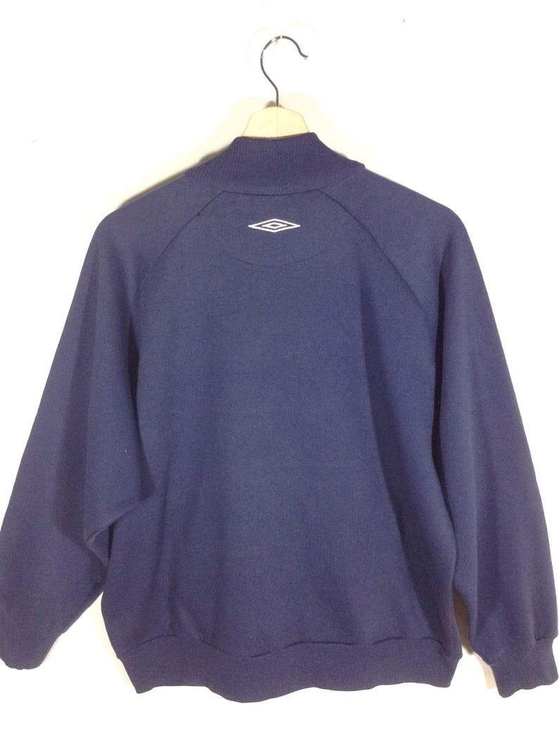 Pu&ograve; includere: Una felpa blu navy con un logo a forma di diamante bianco sul retro.