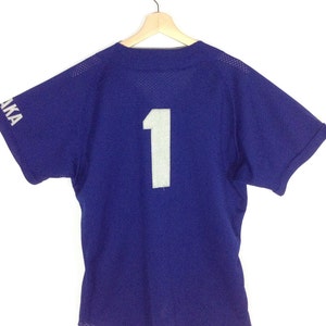May include: A royal blue baseball jersey with a white number "1" on the back. The jersey has short sleeves and a mesh fabric.