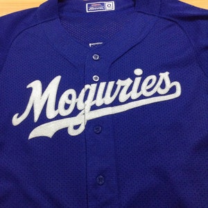 May include: A royal blue baseball jersey with white lettering that reads "Moguries". The jersey has a button-up front and a mesh fabric.
