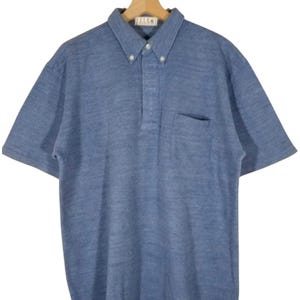 May include: A blue short-sleeved collared shirt with a button-up front and a single pocket on the left side. The shirt has a subtle textured pattern.