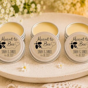 May include: Three round silver metal tins containing yellow lip balm. Each lid features a black graphic of a bee with a dotted flight path, the text "Meant to Bee", and the personalized names "Sarah & Daniel" with the date "4th Jul 2027".
