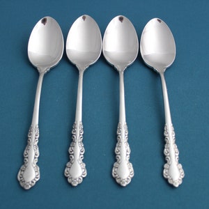 May include: Four silver spoons with ornate handles on a blue background.