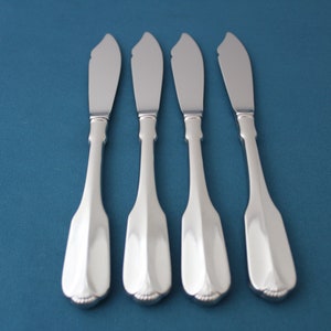 May include: Four silver butter knives with ornate handles arranged in a row on a blue background.