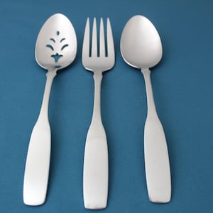 May include: A set of three silver-toned serving utensils, including a slotted spoon, a fork, and a spoon. The utensils are arranged in a row on a blue background.