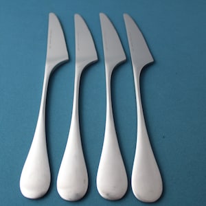 May include: Four silver dinner knives with curved handles on a blue background.