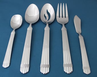 May include: Five silver-toned flatware pieces with a fluted design on the handles. The set includes a spoon, a fork, a butter knife, a serving spoon, and a slotted serving spoon.