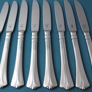 May include: Eight silver dinner knives with a simple, elegant design. The knives have a slightly curved handle and a pointed tip.