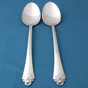 May include: Two silver spoons with ornate handles on a blue background.