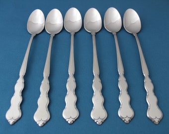 May include: Six silver spoons with ornate handles on a blue background.