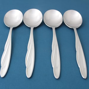 May include: Four silver soup spoons with a decorative design on the handle. The spoons are arranged in a row on a blue background.
