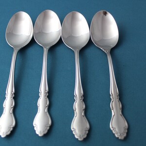 May include: Four silver spoons with ornate handles on a blue background.