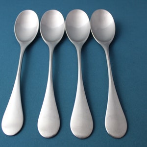 May include: Four silver spoons with rounded bowls and long, slender handles are arranged in a row on a blue background.