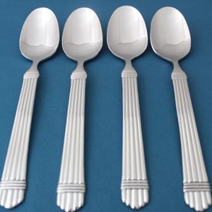 May include: Four silver spoons with a decorative, fluted design on the handle. The spoons are arranged in a row on a blue background.