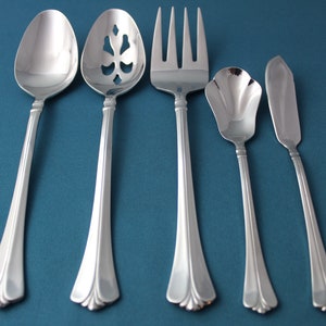 May include: Five silver-toned serving utensils on a teal background. The utensils include a slotted spoon, a spoon, a fork, a butter knife, and a sugar spoon.