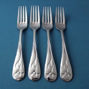 May include: Four silver forks with floral designs on the handles. The forks are arranged in a row on a blue background.