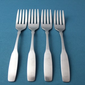 May include: Four silver forks are lined up in a row on a blue background. The forks are all the same size and shape, and they are all pointing in the same direction.