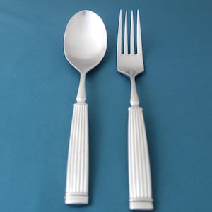May include: Silverware set featuring a spoon and fork. The spoon has an oval bowl, and the fork has four tines. Both utensils have long, ridged handles with a decorative design. The background is a solid teal color.