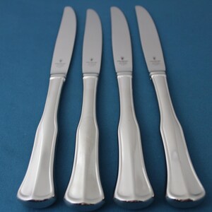 May include: Four silver dinner knives with a polished finish and rounded handles.