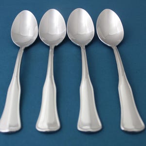 May include: Four silver spoons with a simple, elegant design. The spoons are arranged in a row on a blue background.