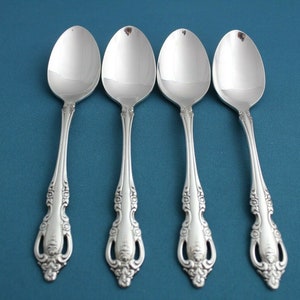 May include: Four silver spoons with ornate handles on a blue background.