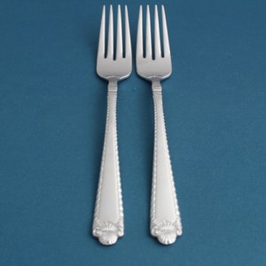 May include: Two silver forks with ornate handles on a blue background.