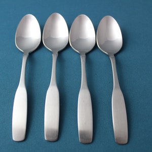May include: Four silver spoons lined up on a blue background.