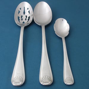 May include: Three silver spoons, one with a decorative scalloped edge, one with a scalloped edge and openwork design, and one with a plain round bowl.