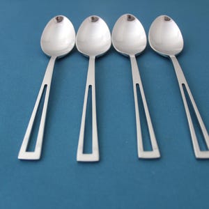 May include: Four silver spoons with a polished finish are arranged in a row on a blue surface.
