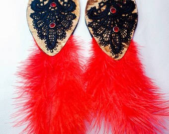 May include: A pair of long, dangling earrings with a cork base, black lace, and red rhinestones. The earrings are adorned with bright red feathers.
