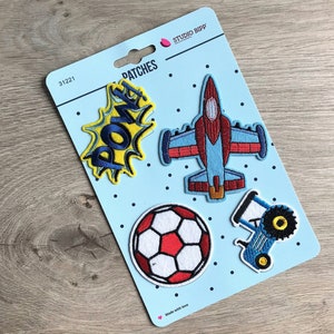 Könnte beinhalten: Ein Set mit vier Bügelbildern auf blauem Hintergrund mit weißen Punkten. Die Patches beinhalten ein rotes und blaues Flugzeug, einen blauen Traktor, eine gelbe und blaue "POW"-Grafik und einen roten und weißen Fußball. Die Verpackung trägt die Aufschrift "Patches" und "Studio Bipp".