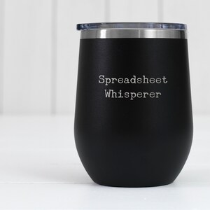 May include: Black stainless steel tumbler with a white inscription that reads "Spreadsheet Whisperer".