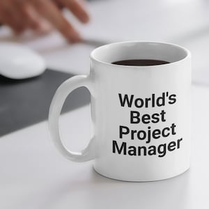 May include: White ceramic coffee mug with black text that reads "World's Best Project Manager".