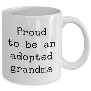 May include: White ceramic coffee mug with black text that reads "Proud to be an adopted grandma".