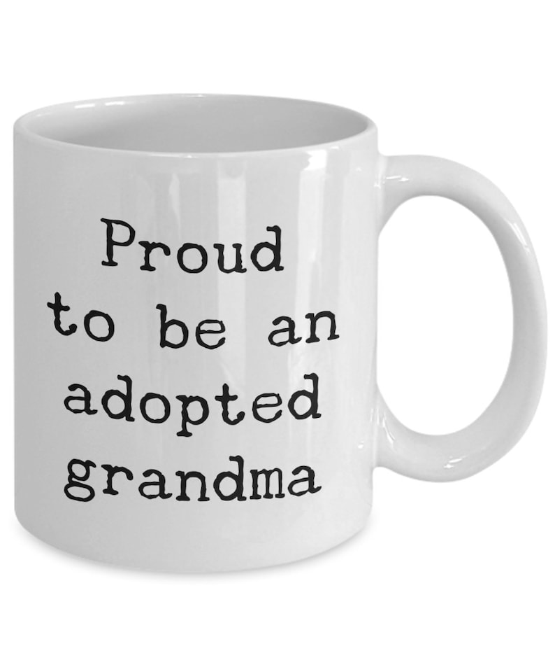 May include: White ceramic coffee mug with black text that reads "Proud to be an adopted grandma".