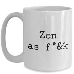 May include: White ceramic mug with a black handle. The mug features the text "Zen as f*&k" in a bold, typewriter-style font. The design is centered on the mug's surface.