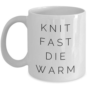 May include: White ceramic mug with black text that reads "Knit Fast Die Warm".